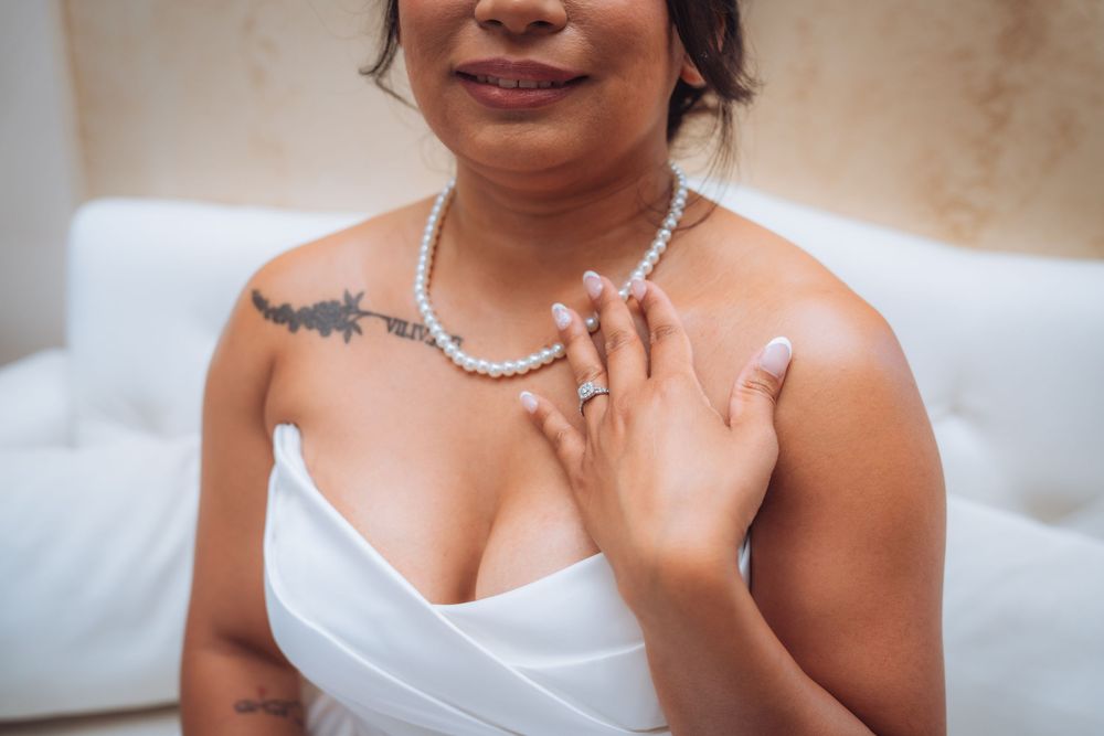 Bride in white strapless gown wearing pearl necklace and ring, with floral shoulder tattoo.