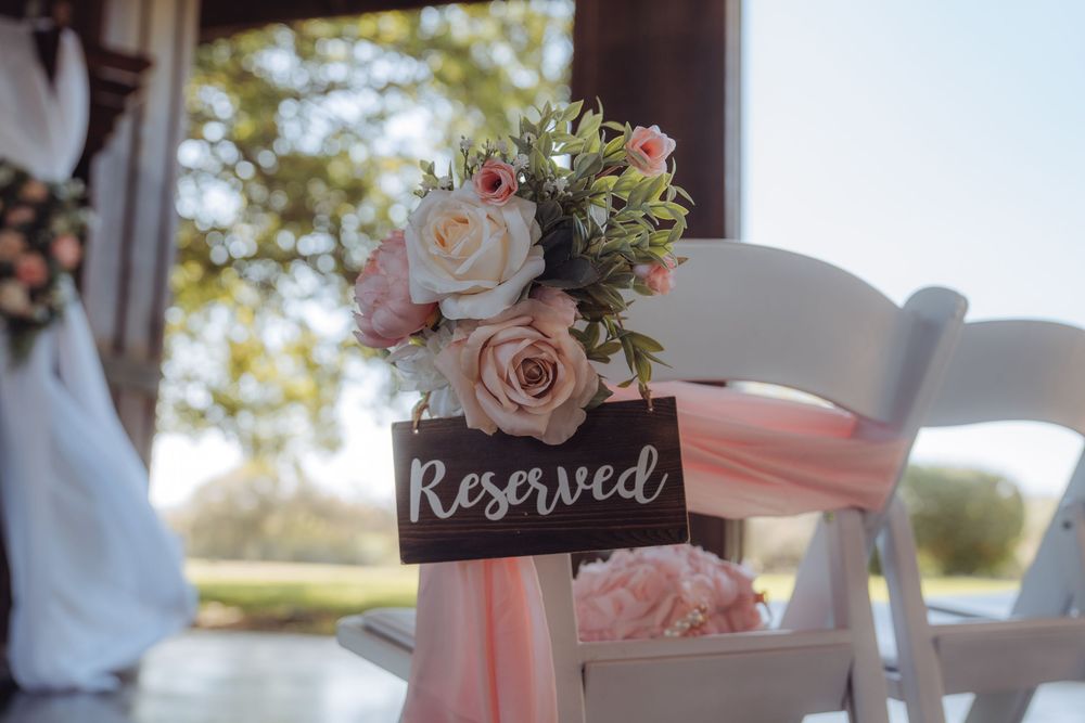 White wedding chair with reserved sign adorned with blush pink and cream roses and pink ribbon.