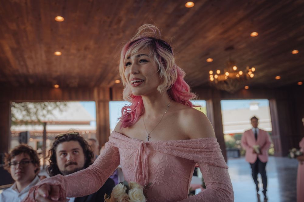 Woman with pink hair in an off-shoulder pink dress at an elegant indoor wedding reception venue.
