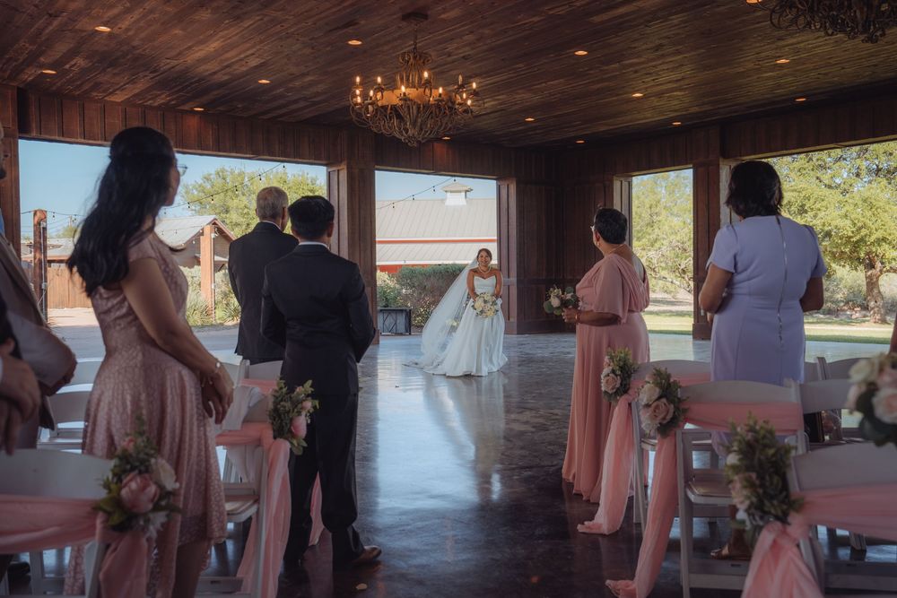 Bridesmaids in blush pink dresses stand as bride walks down aisle in elegant rustic wedding venue.