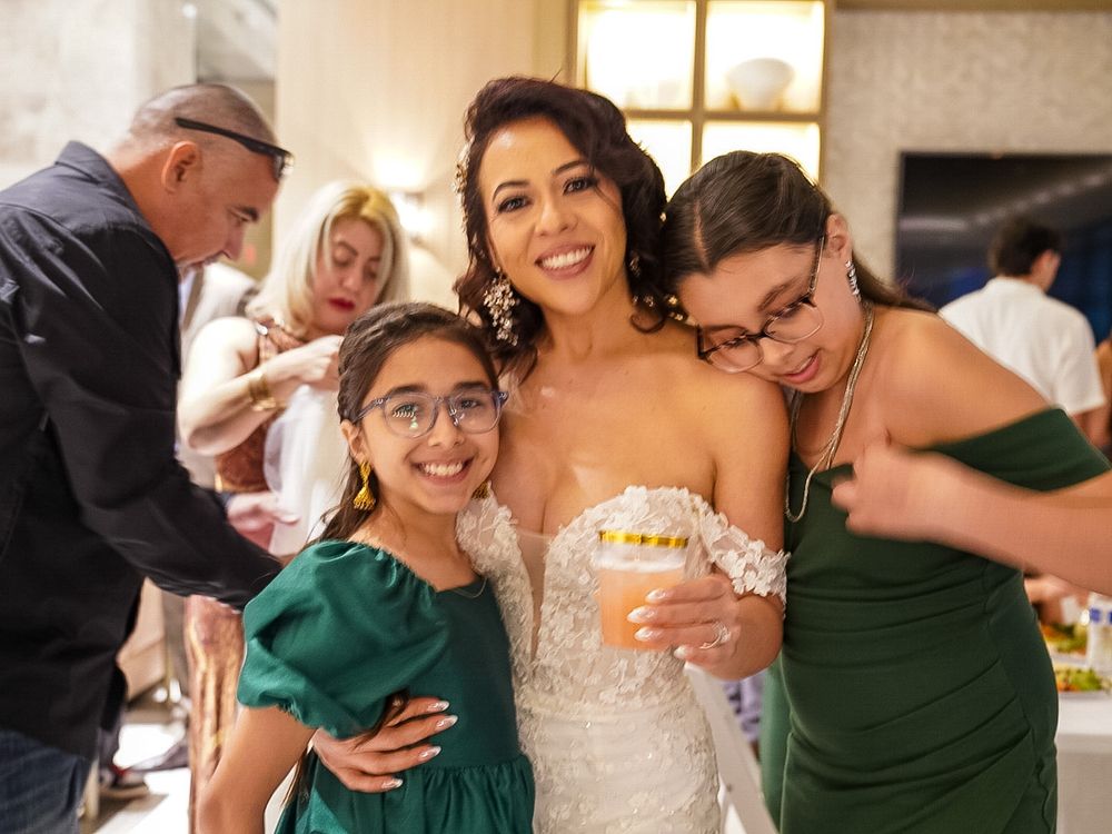 Bride in white gown smiling with two girls in green dresses at a wedding reception celebration.