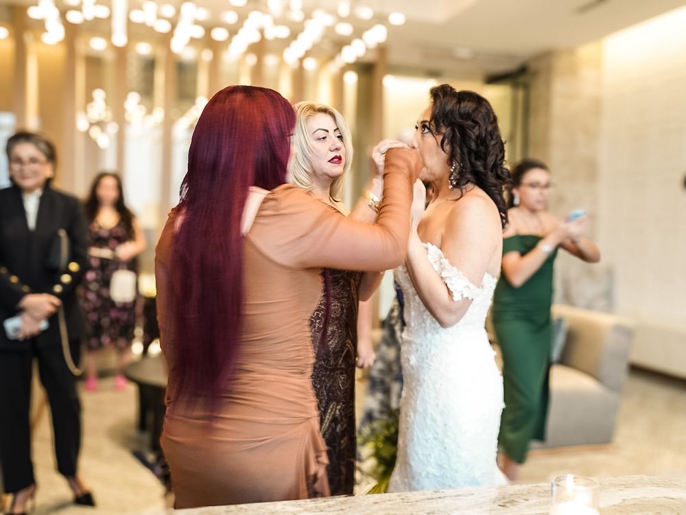 Woman in bridal gown receives makeup touch-up from red-haired woman in tan dress at elegant wedding reception.