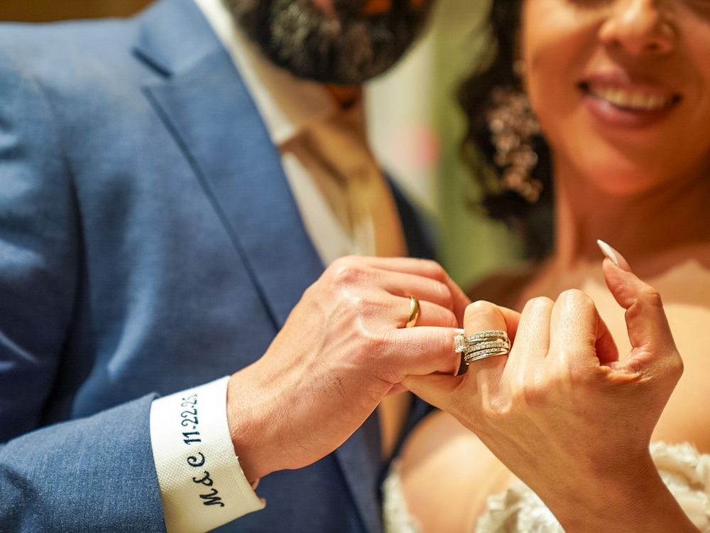 Close-up of groom placing wedding ring on brides finger during ring exchange ceremony.