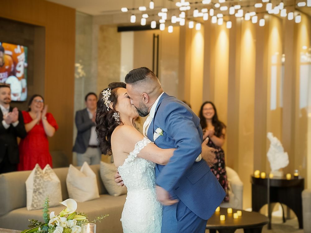 Bride and groom share first kiss at wedding ceremony while guests applaud in elegant venue.