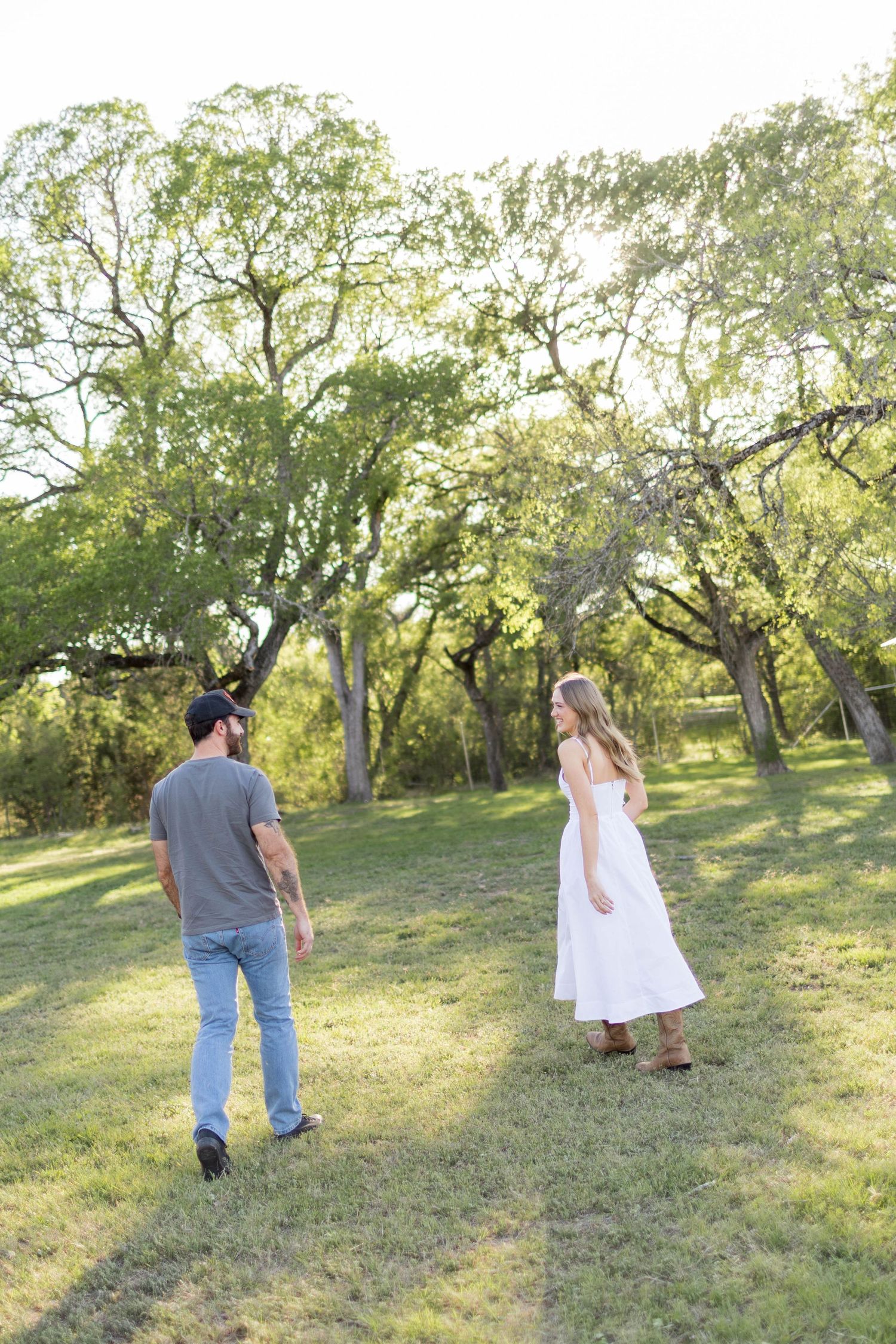 A man lifts and spins a woman in a white dress outdoors, sharing a romantic kiss at Commons Ford Ranch in Austin, Texas.