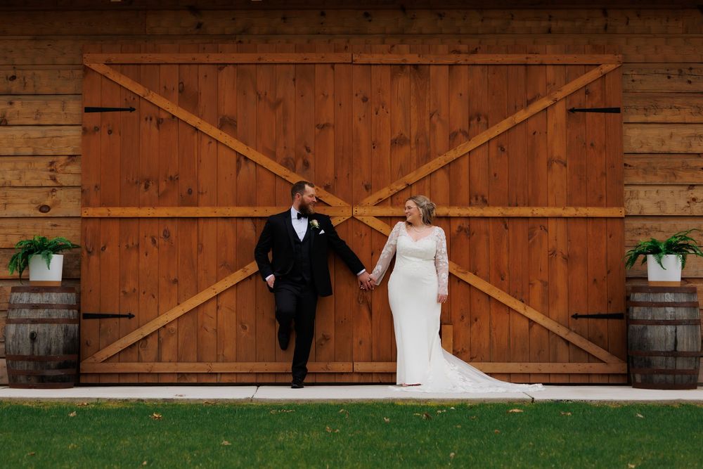 Bride and groom holding hands walking in front of rustic wooden barn doors at outdoor wedding venue.