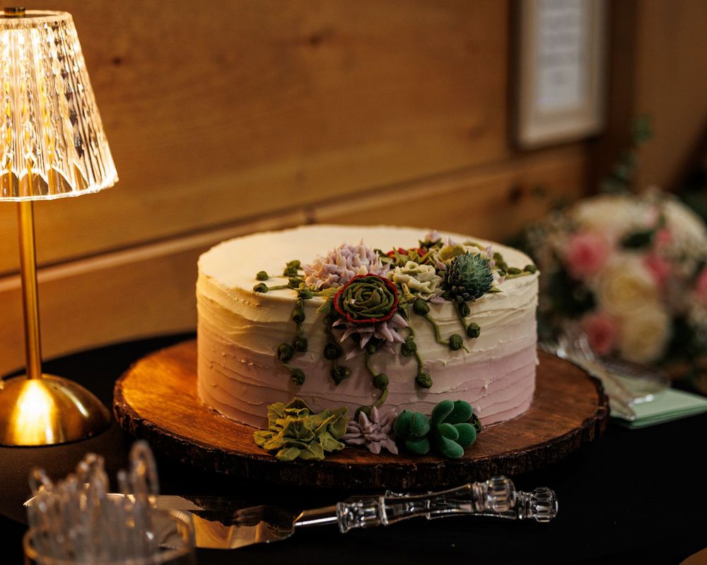 Elegant white ombre wedding cake with succulent decorations on a rustic wood slice stand, illuminated by a crystal lamp.