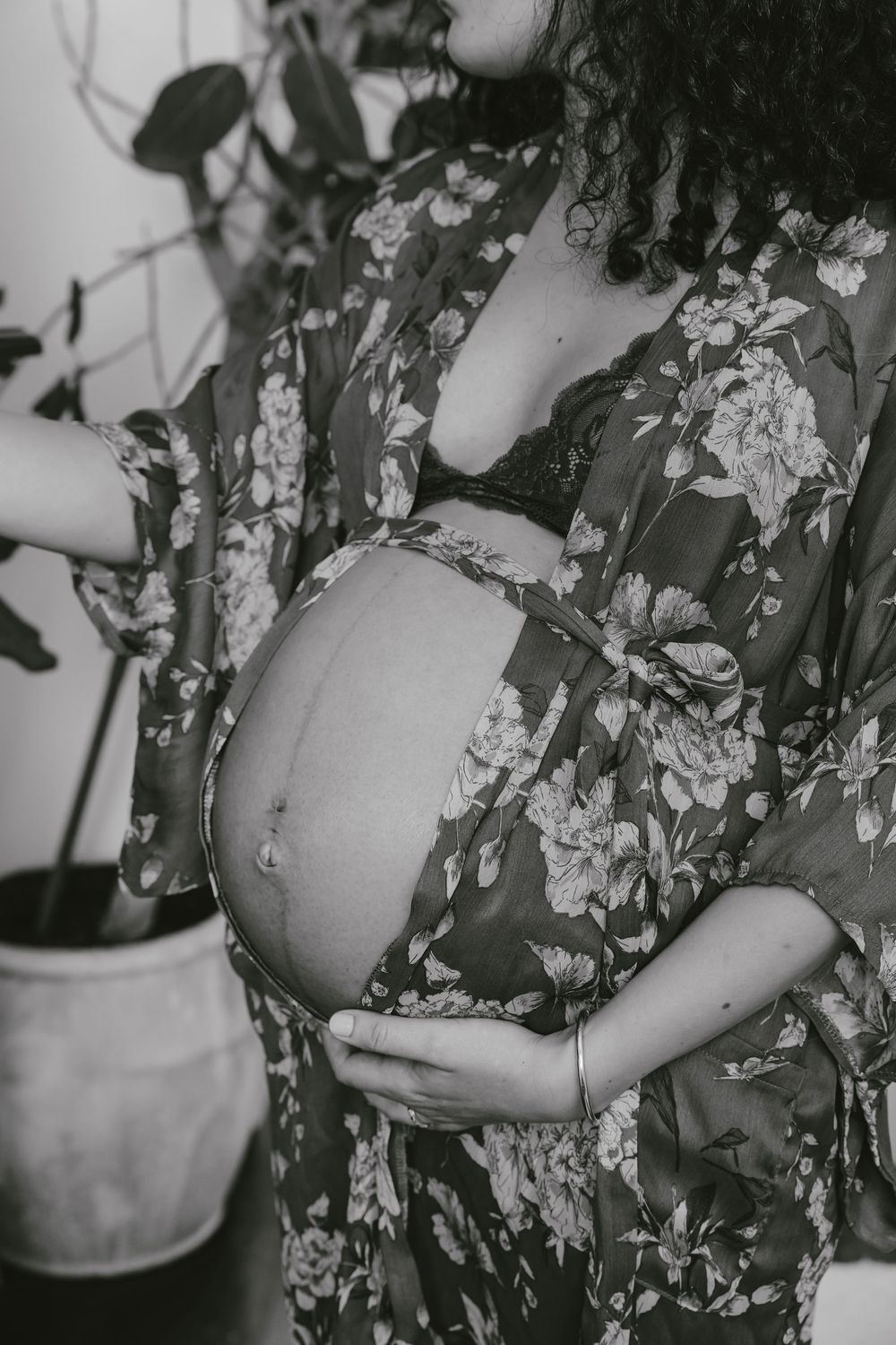 Black and white photo of pregnant woman in floral robe cradling baby bump.