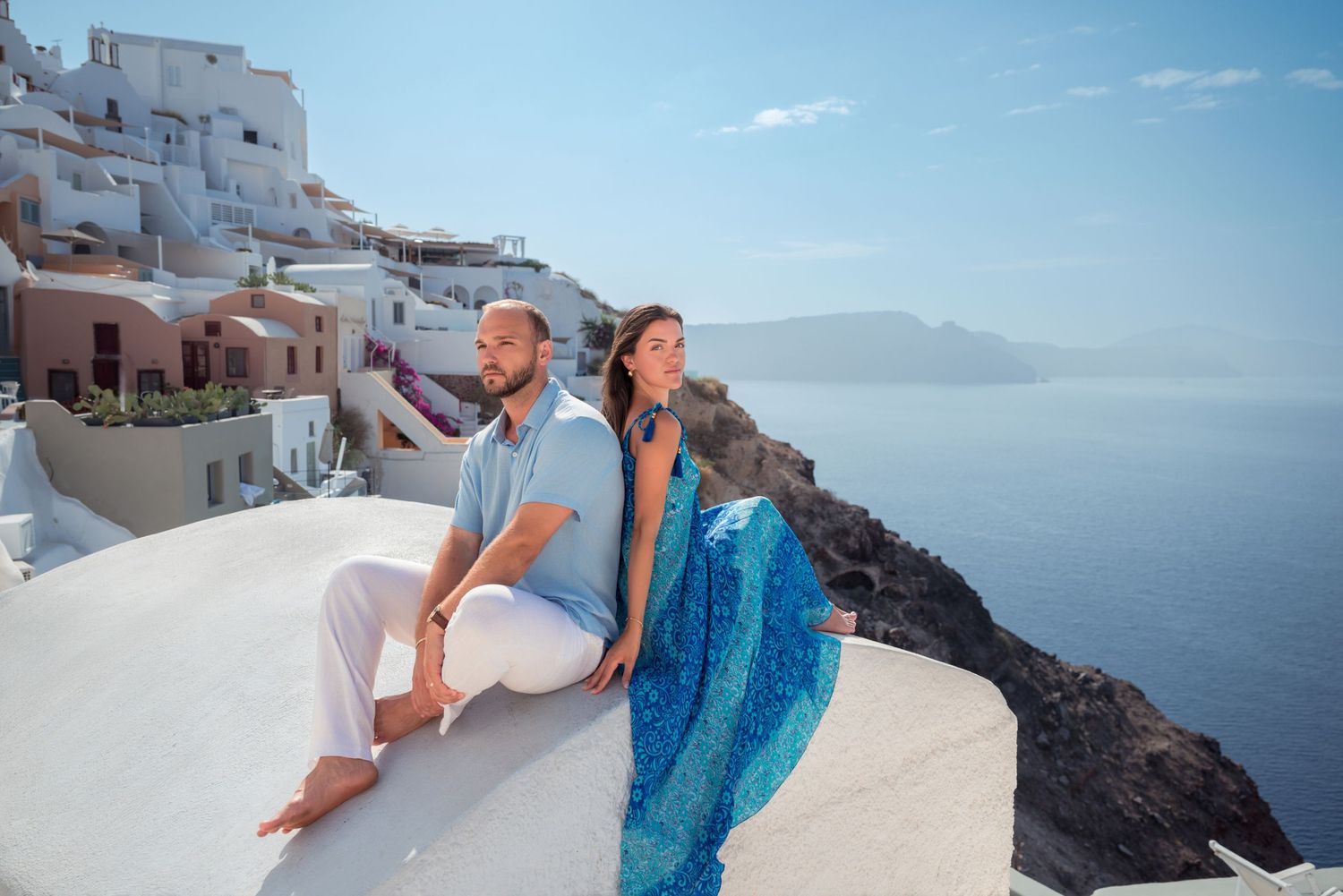 Couple holding hands walking on white terrace in Santorini Greece with blue sky and caldera views.