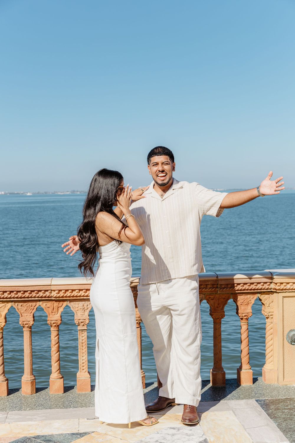 Joyful couple posing on a decorative terrace overlooking the ocean on a sunny day.