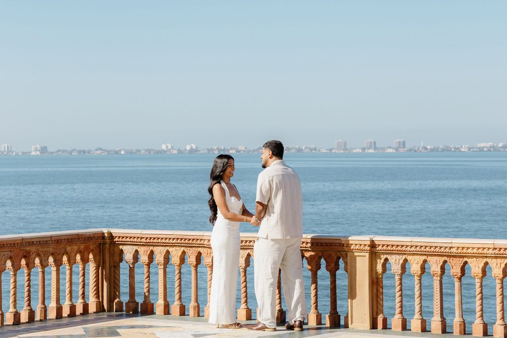 Couple in white standing face to face on marble terrace overlooking calm blue sea.