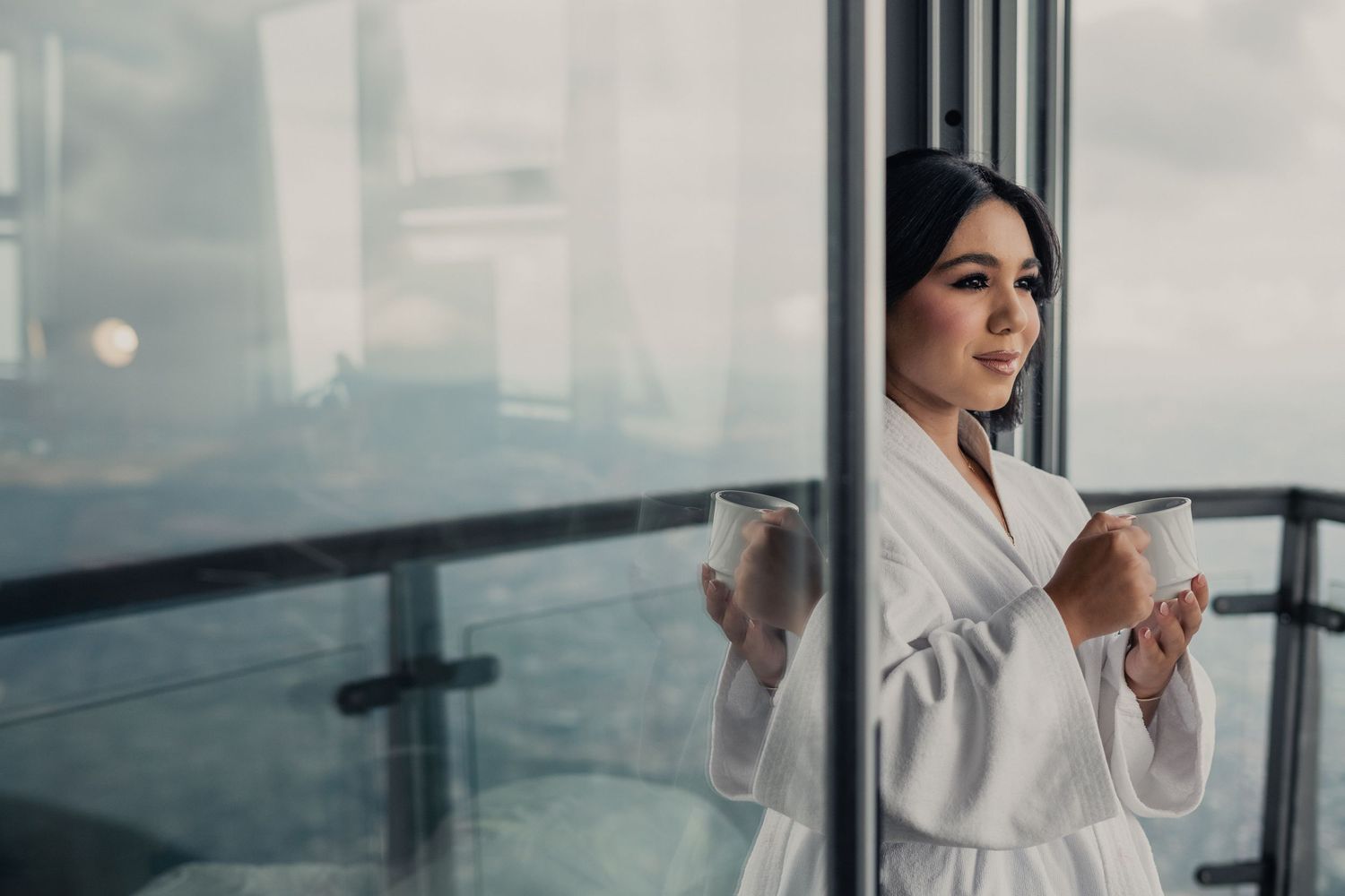 Professional in a white bathrobe stands thoughtfully by large windows in a modern hotel room.