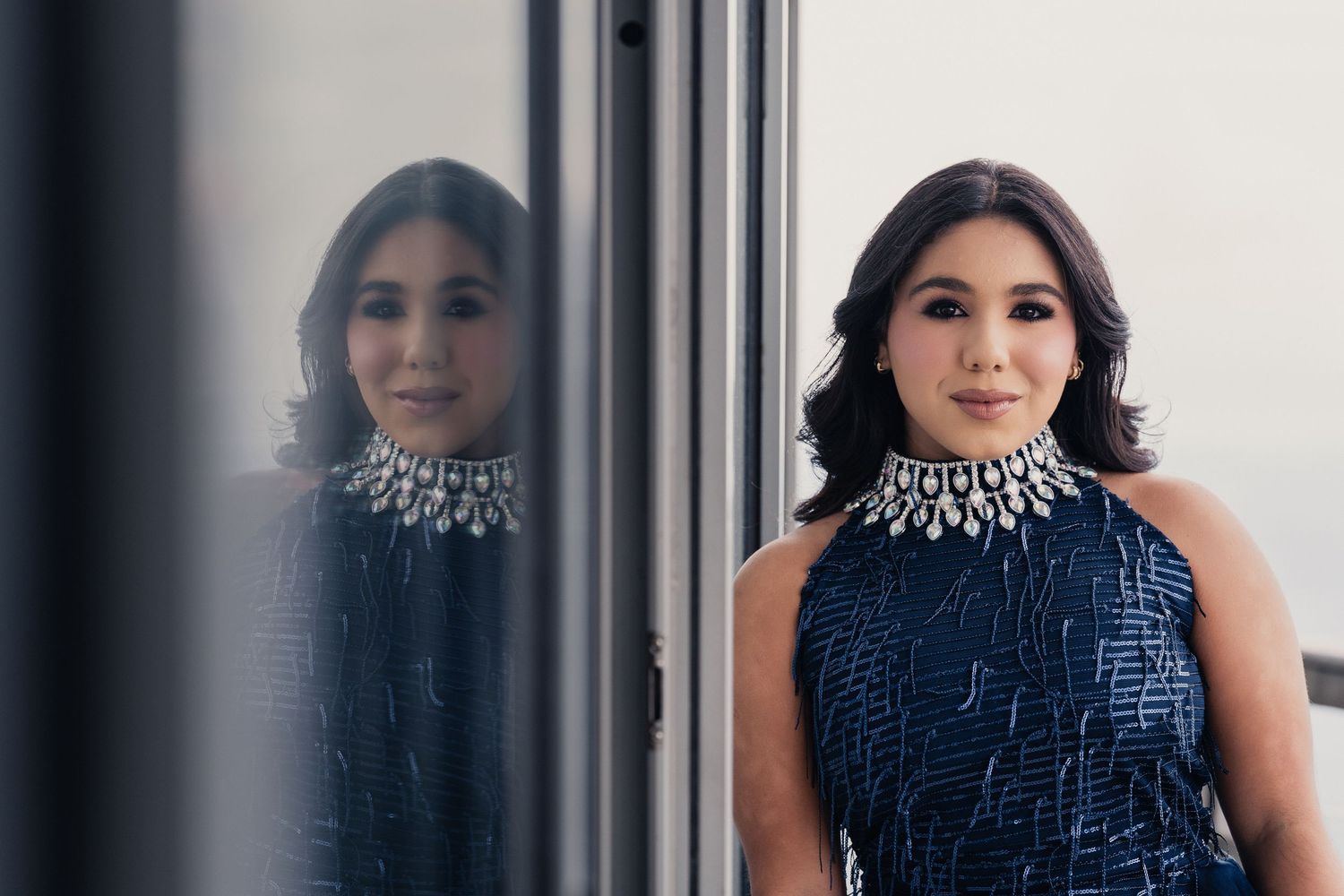 A person wearing a navy blue dress with white beaded neckline poses in different positions against a light background.