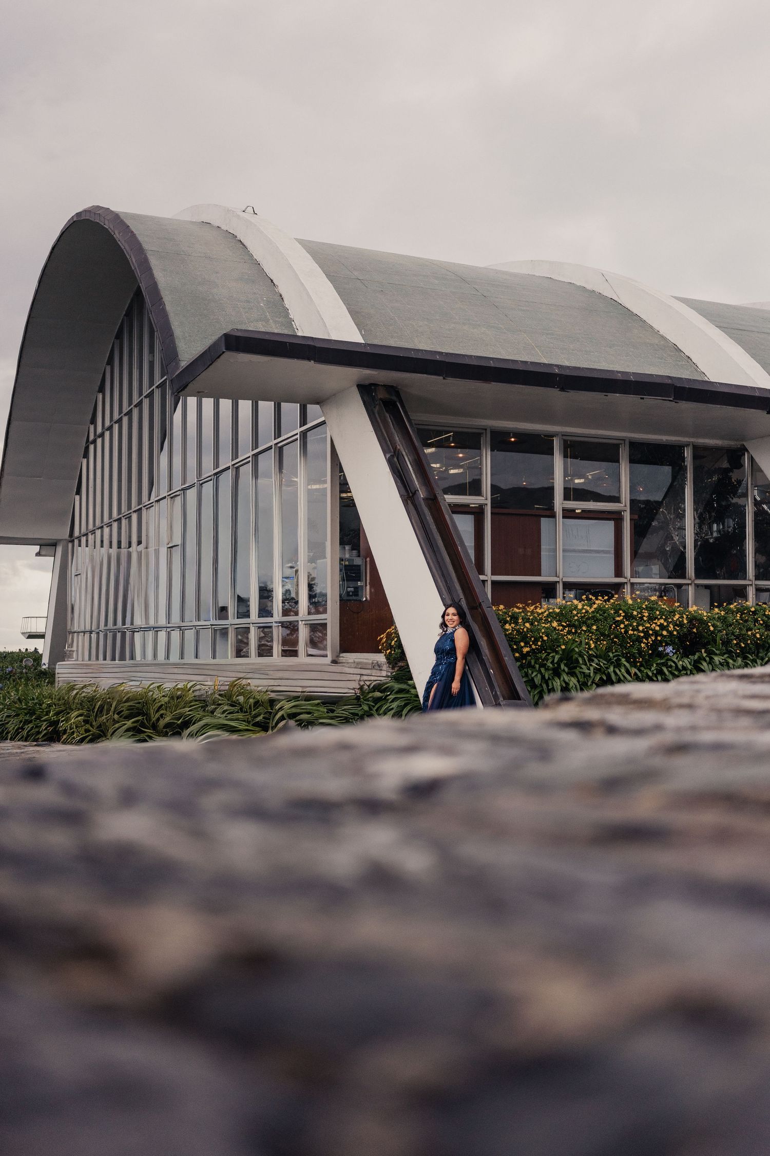 Modern curved roof architecture building with glass windows and angled support beams against cloudy sky.