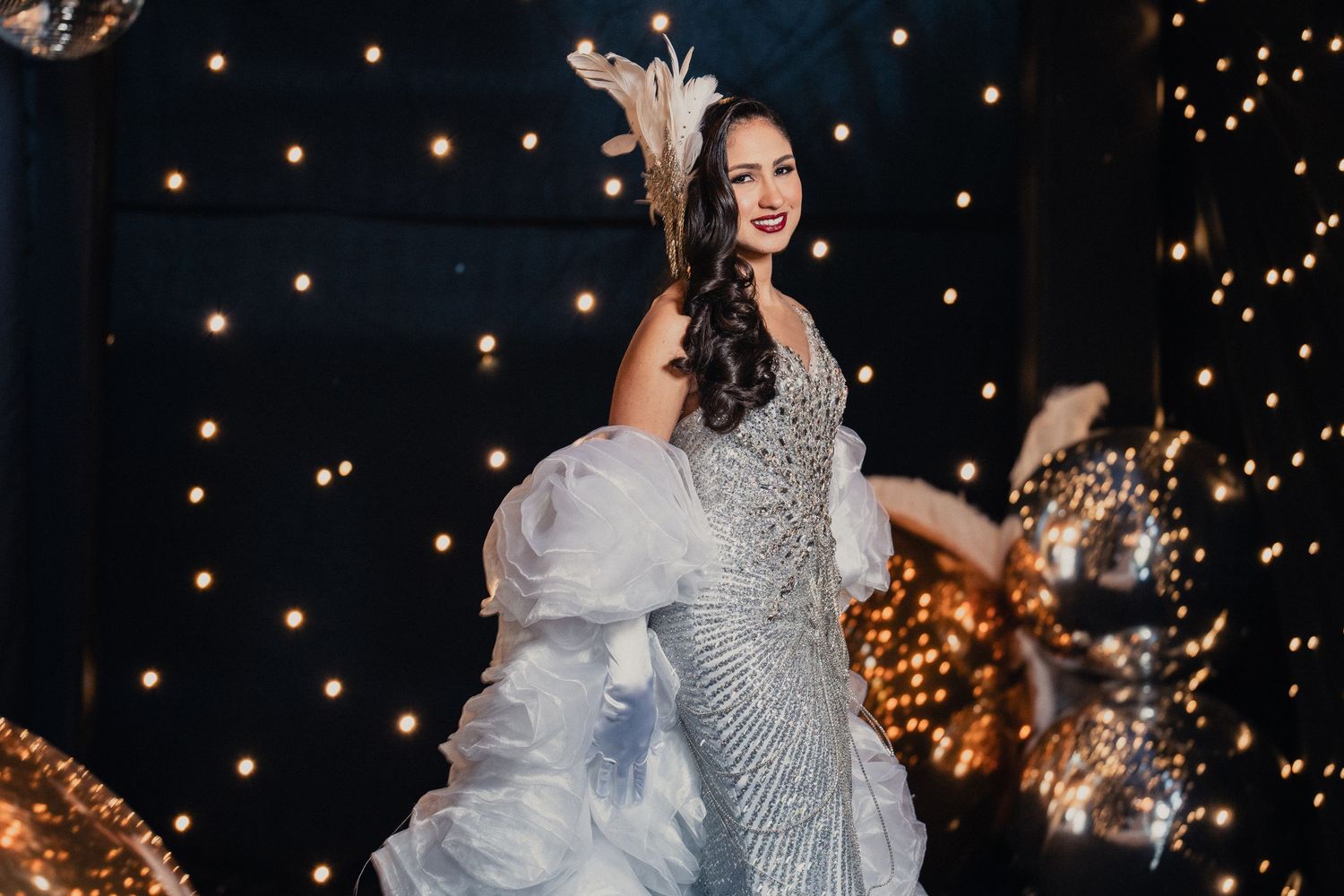 A bride in a sparkly silver dress twirls on the dance floor with twinkling lights in the background.