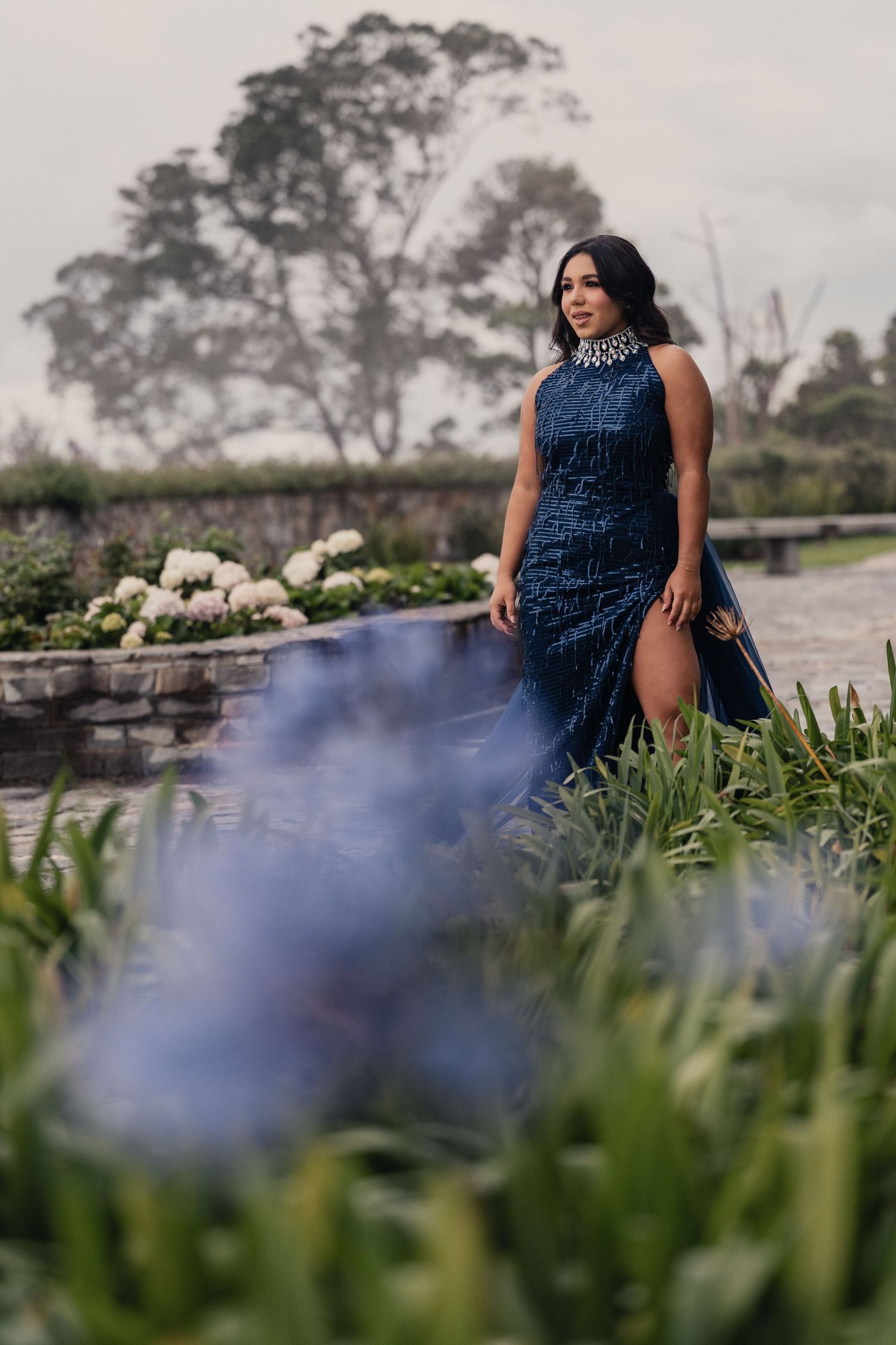 Blue evening gown flowing in garden setting with hydrangea flowers and stone wall.