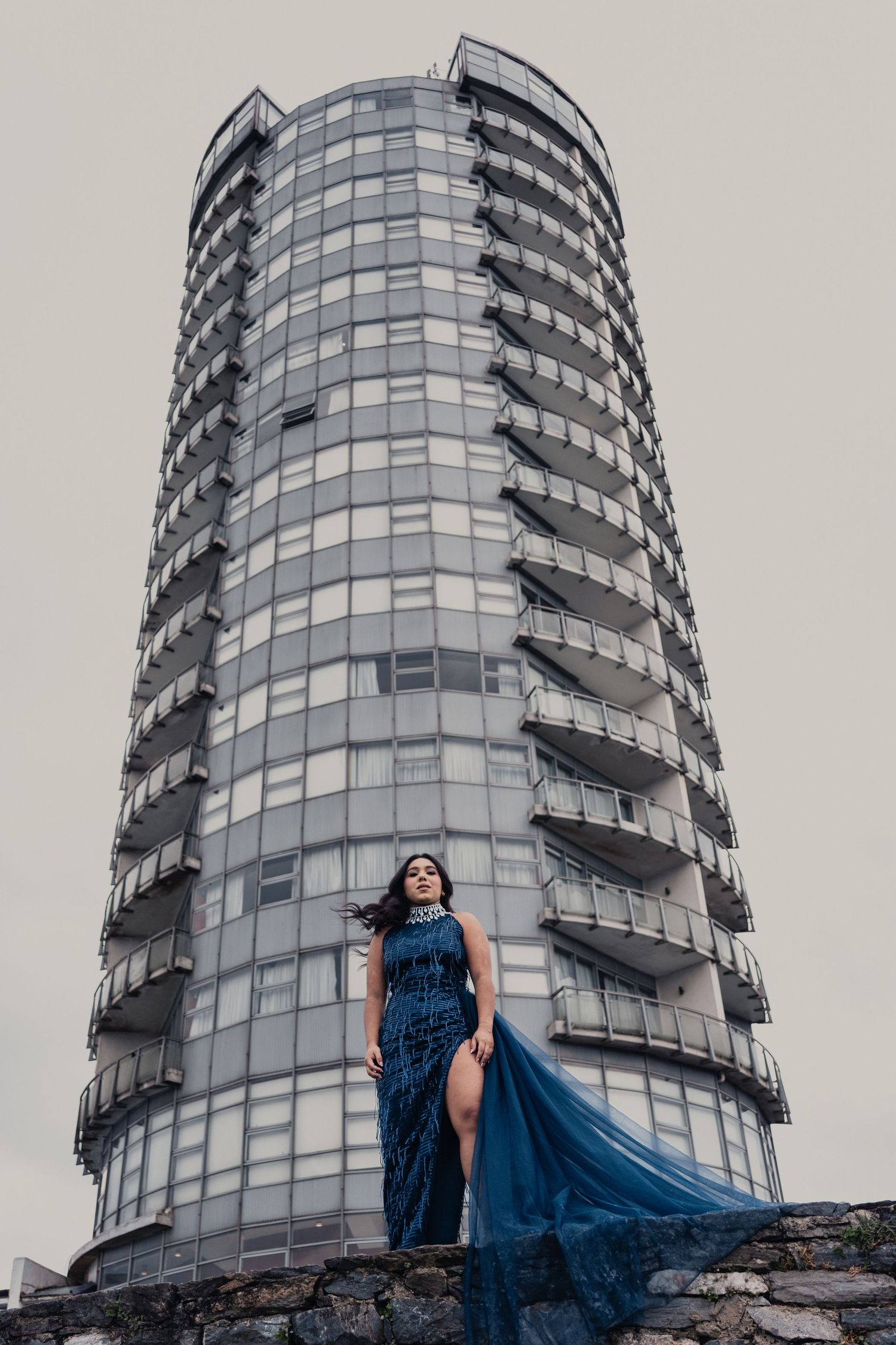 Dramatic fashion photo against modern glass high-rise building with curved architecture.