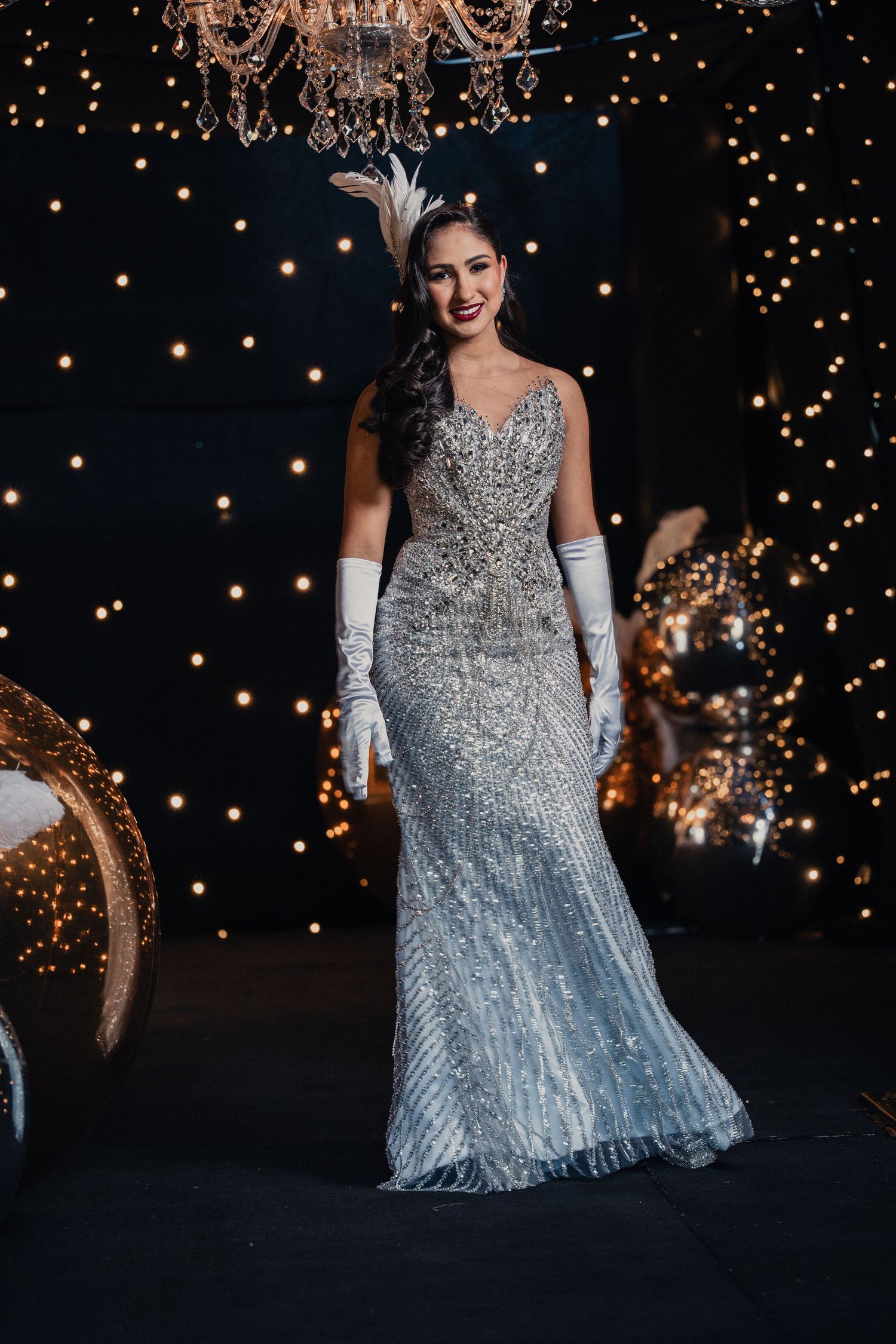Glamorous evening scene with sparkly silver gown against backdrop of twinkling lights and crystal chandelier.