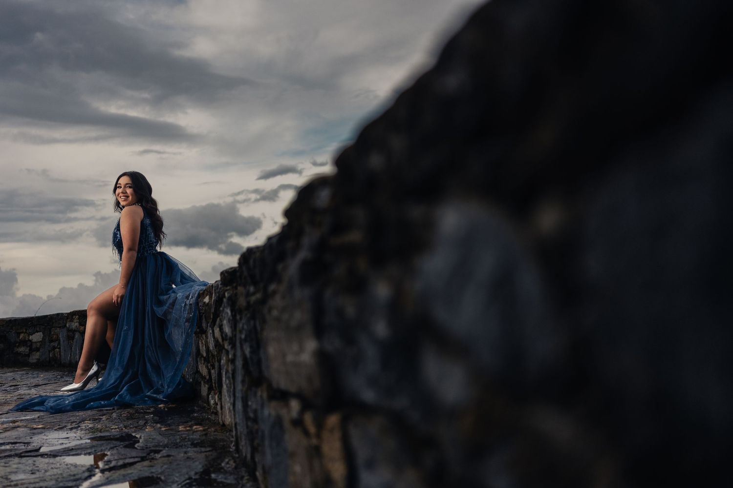 A dramatic series of photos showing a figure in a blue dress against a moody cloudy sky on a coastal cliff.