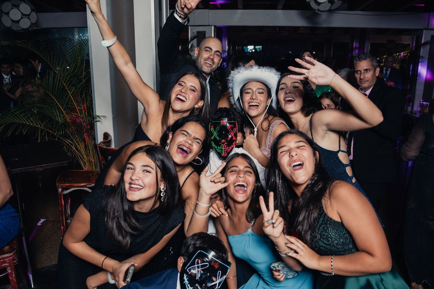 Friends posing together and making peace signs while celebrating at a dimly lit party venue.
