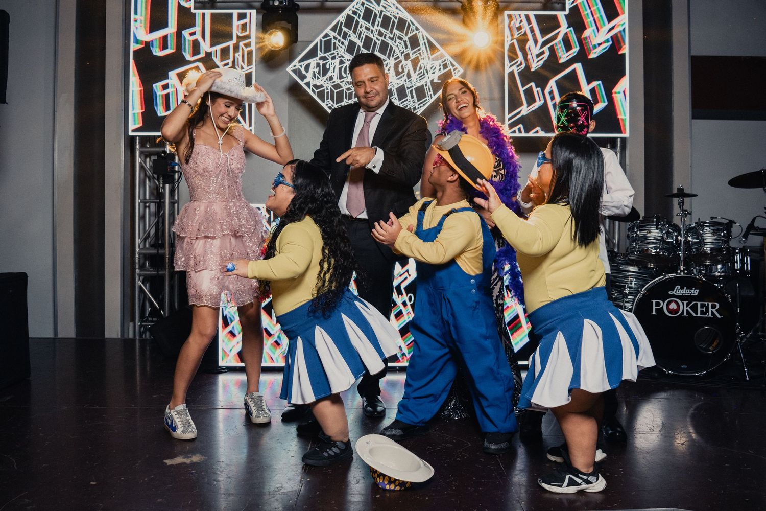 People dancing together at a party with cheerleaders in blue and white uniforms against a decorative backdrop.