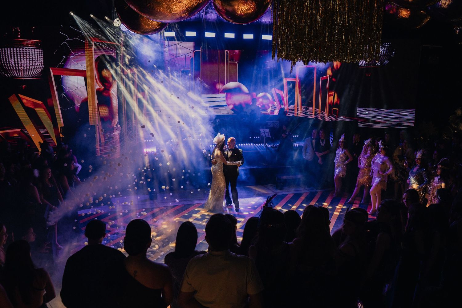 Silhouettes of performers on a dark stage with dramatic blue and purple lighting effects creating an atmospheric scene.