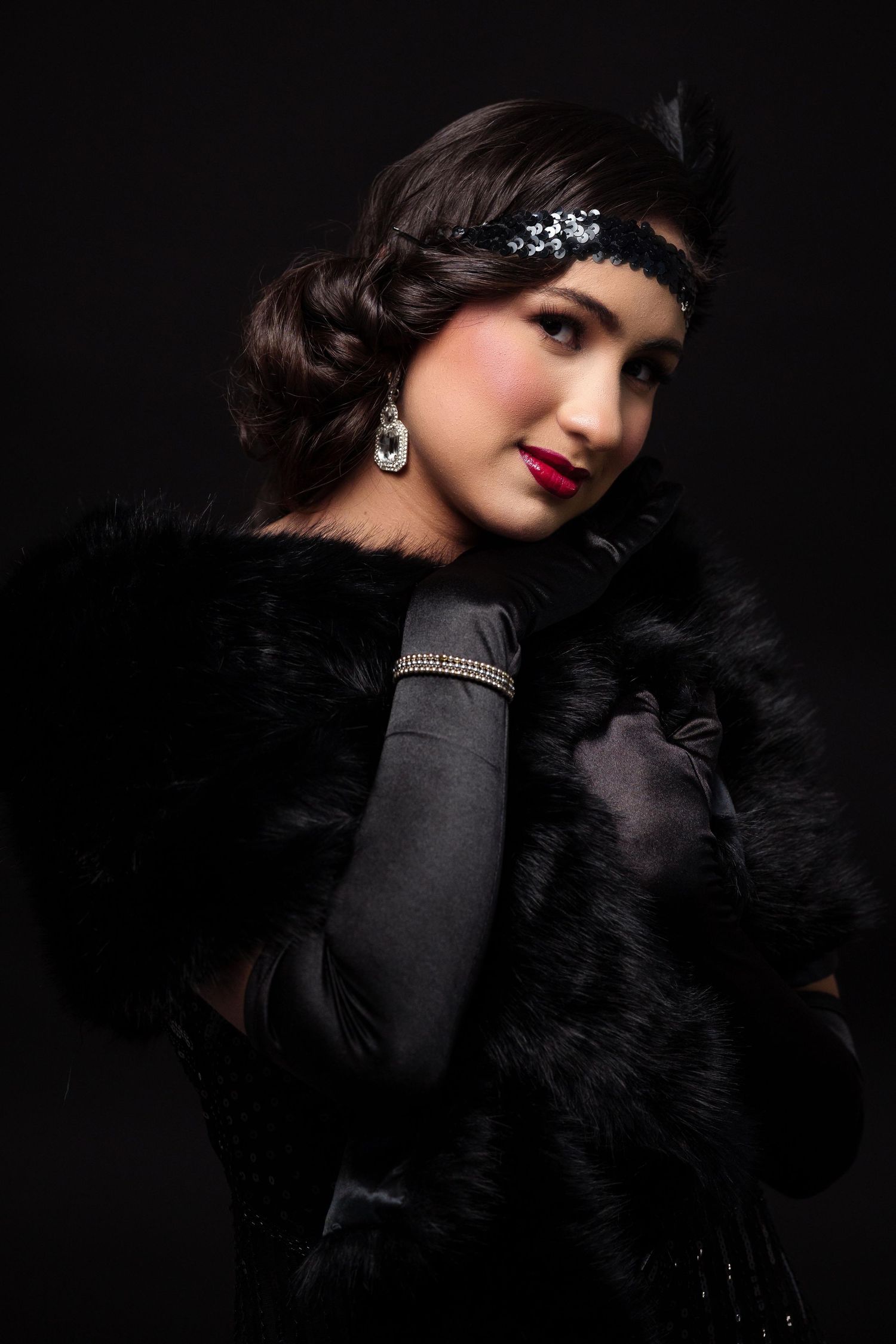 Dramatic fashion portrait with black feathers and red lipstick against dark background.