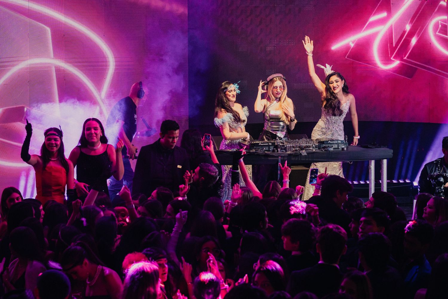 Concert audience in a dark venue illuminated by vibrant pink and purple stage lighting during a live performance.