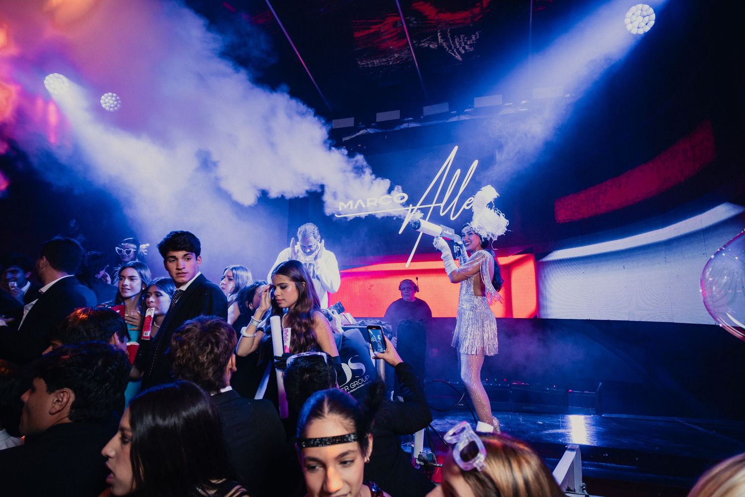 Energetic nightclub scene with bright spotlights and a packed dance floor beneath colorful lighting.