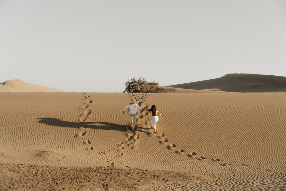 Destination wedding photographer capturing a carefree couple running against the wind in a vast landscape.