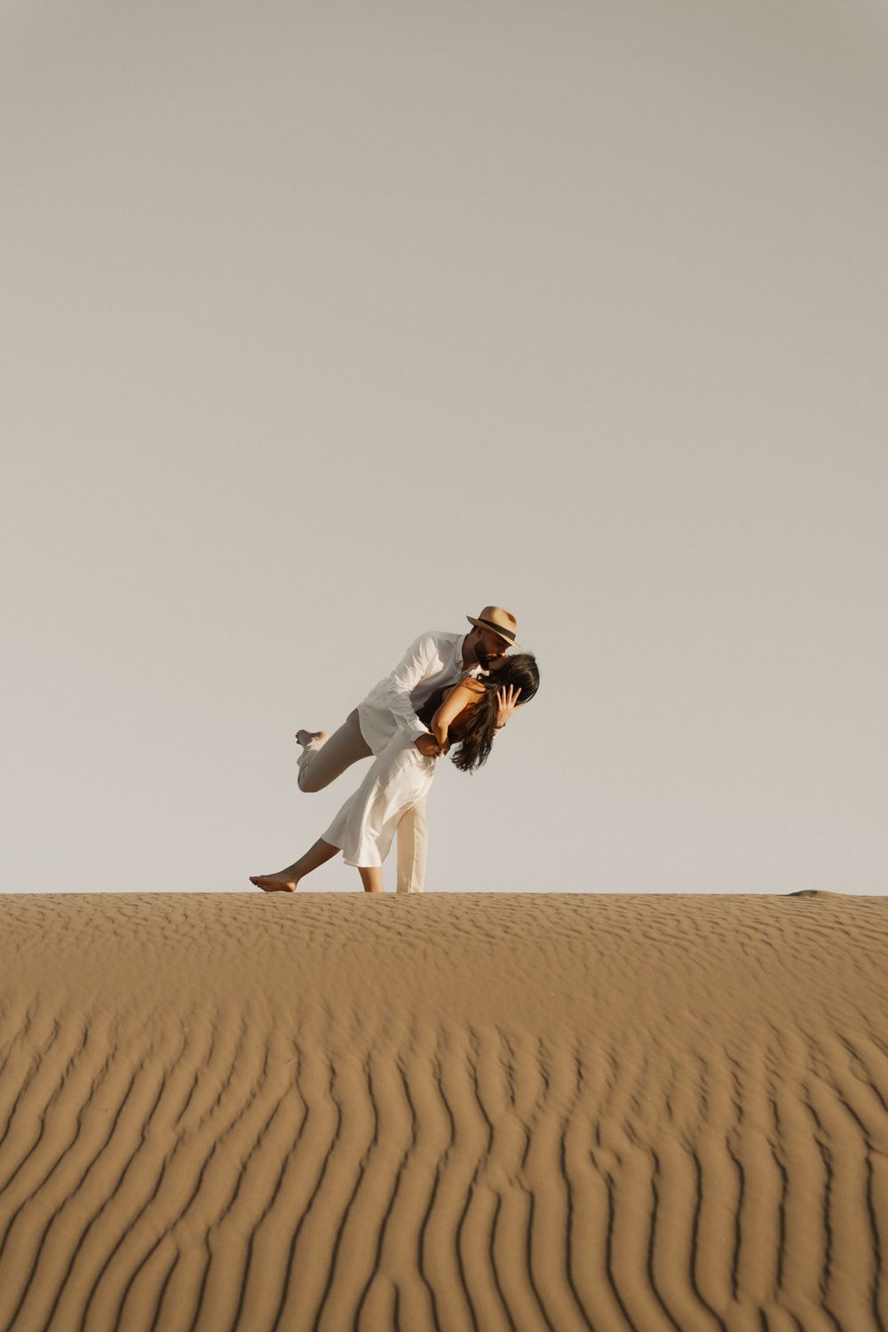 Silhouettes of a romantic couple dancing on a desert ridge at dusk, editorial vibe.