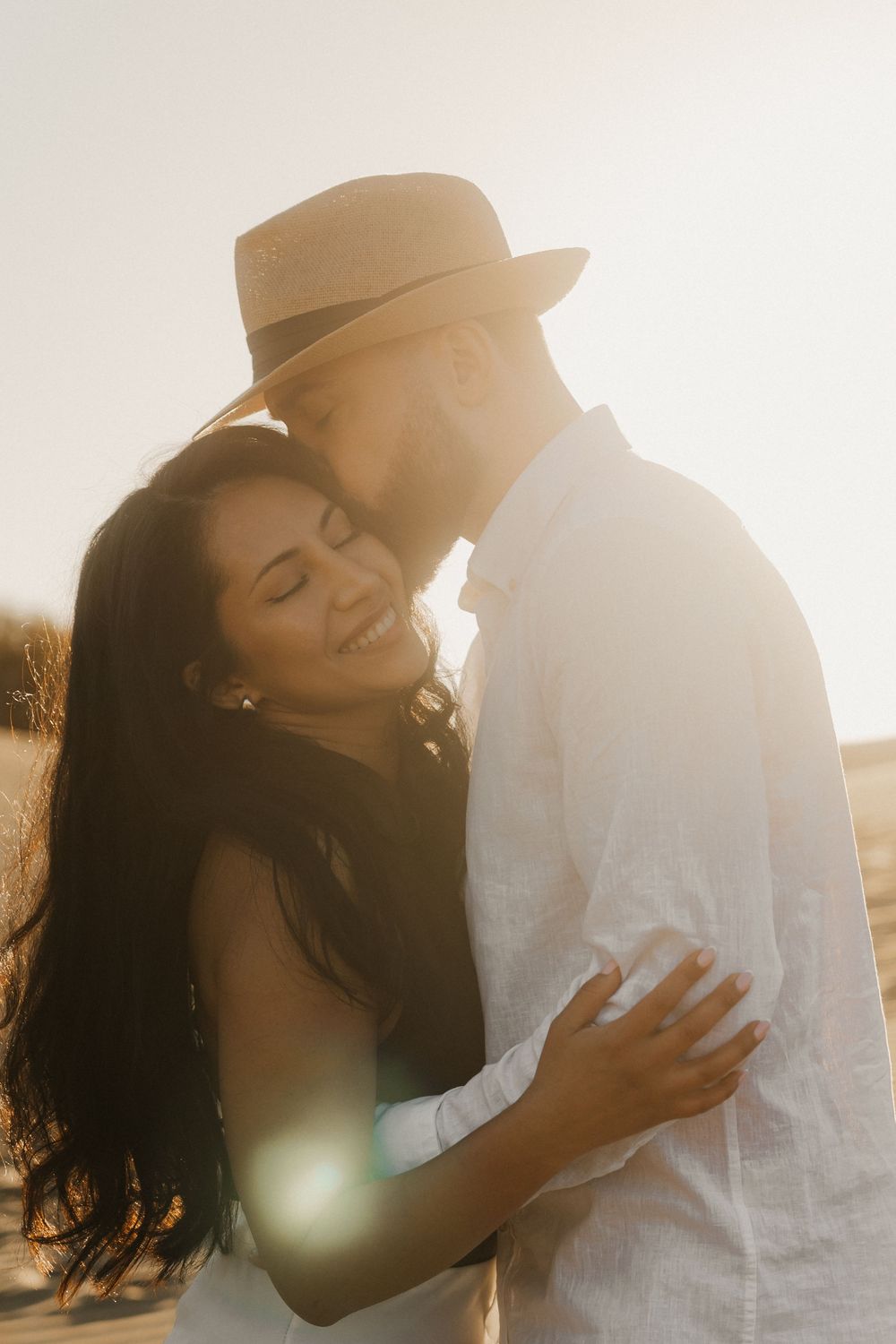 Fine art detail photography of a couple hugging, focusing on the textures of the clothes and sand.