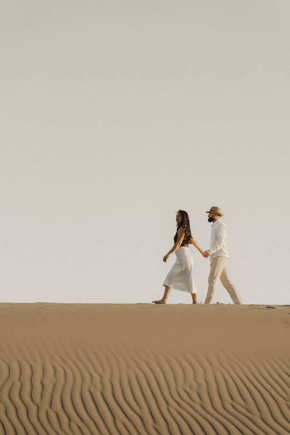 Wide-angle cinematic shot of a couple surrounded by endless sand dunes, destination photography.