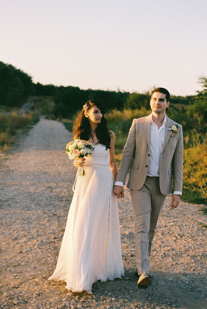 A couple walks hand in hand on a beach path during sunset wearing formal attire.
