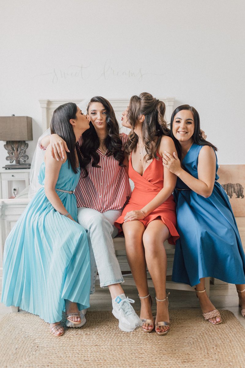 A group wearing coordinating blue and coral dresses sits together on a couch during a wedding celebration.