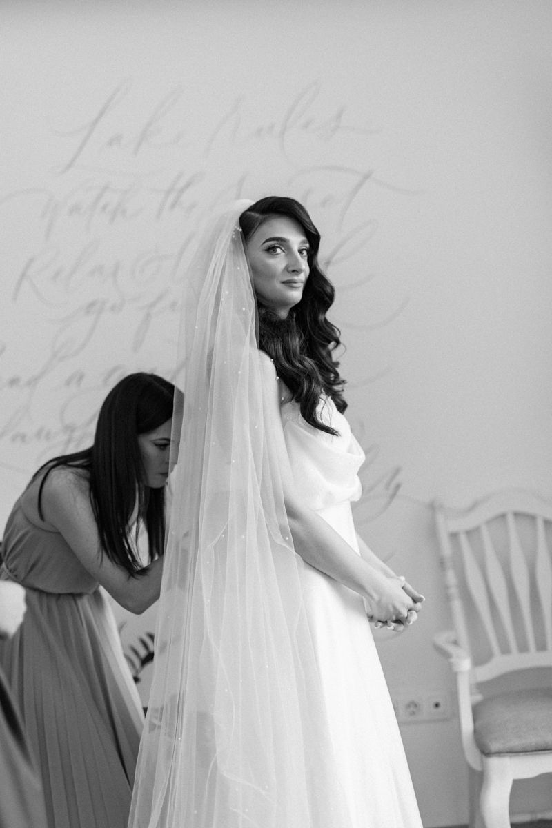 A bridal preparation scene with flowing white wedding dress and attendants in soft lighting.