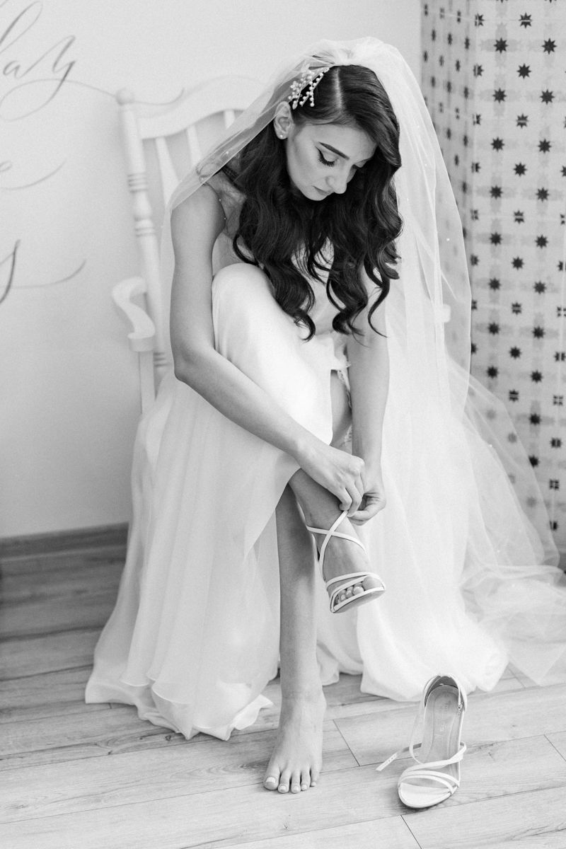 Black and white photo of a bride putting on her wedding shoes before the ceremony.