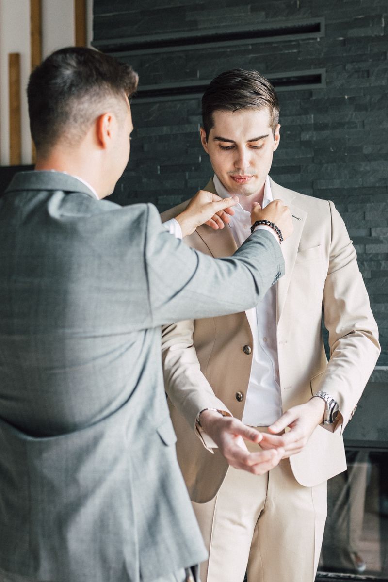 Two people in suits adjusting formal attire before a wedding ceremony.