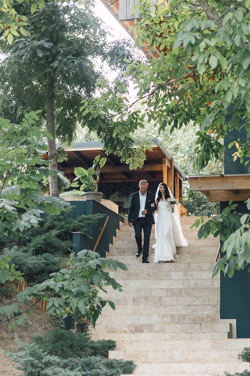 Wedding couple descending stone steps surrounded by lush greenery at an outdoor venue.