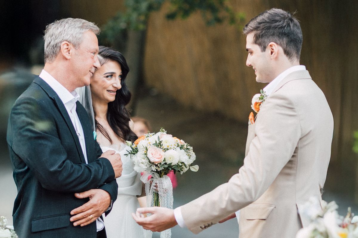 Outdoor wedding ceremony with a wooden arch decorated in peach and coral floral arrangements.