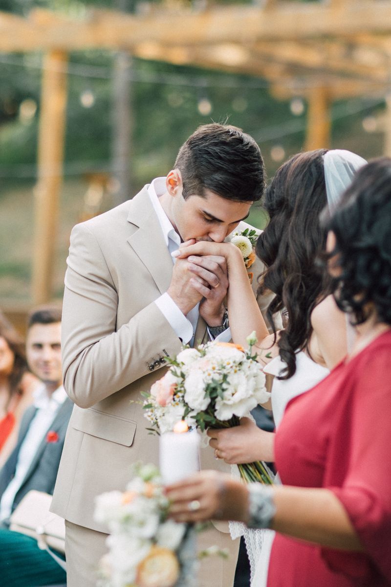 Intimate outdoor wedding ceremony moment under wooden pergola with floral decorations.