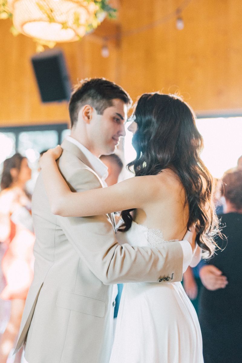 Wedding couples dance together on a wooden floor under warm lighting at an indoor reception.