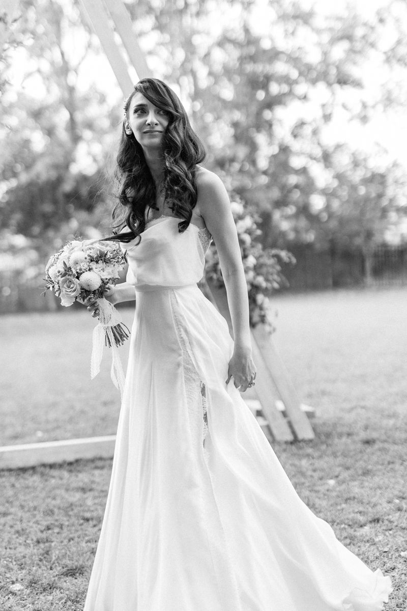 Black and white portrait of bride in flowing wedding dress holding bouquet outdoors.