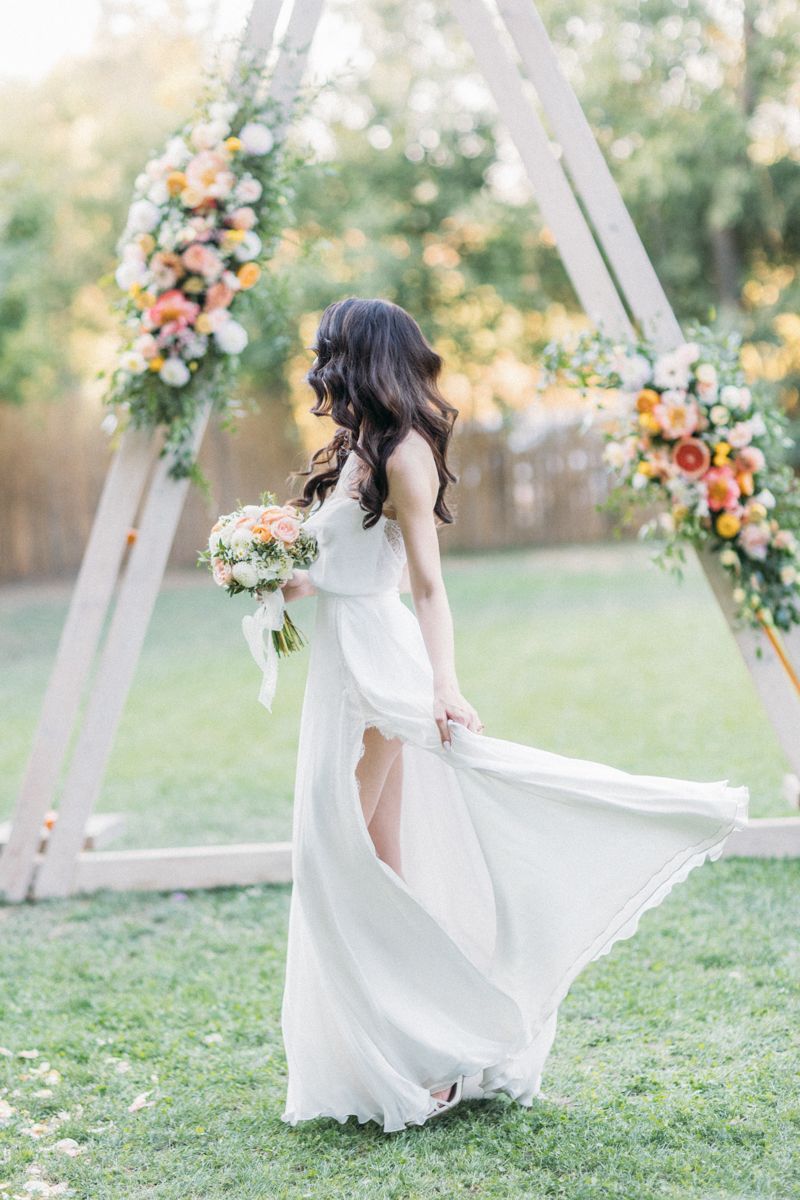 Bride in flowing white dress twirls in garden setting with floral arch backdrop.