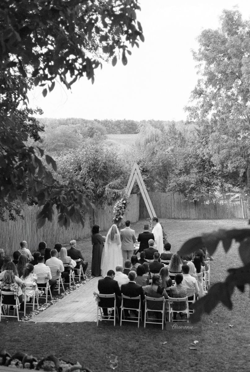An outdoor wedding ceremony setup with white chairs and a wooden arch in a garden setting.
