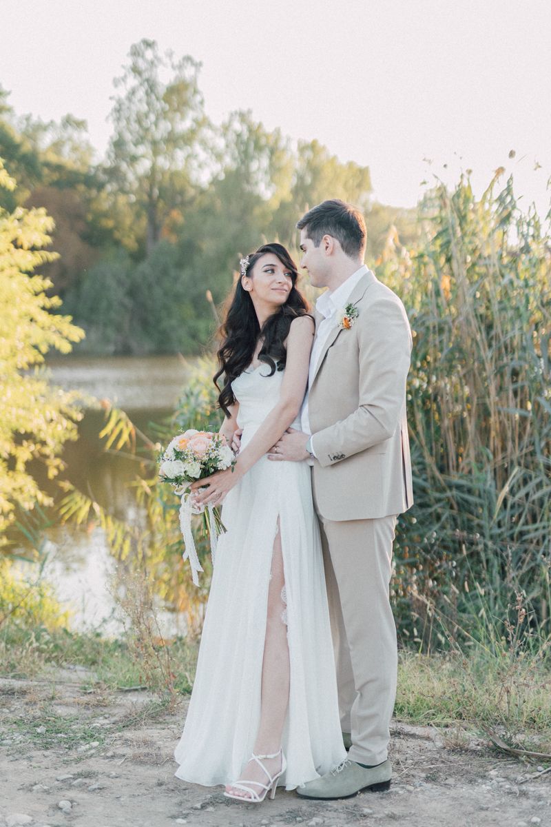 Newlywed couple poses by a lakeside with tall reeds in the background during golden hour.