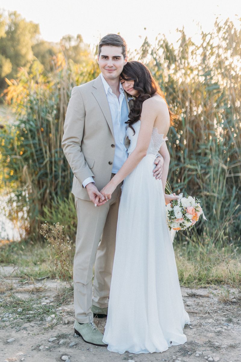 Wedding couple shares intimate moments near a pond with cattails during sunset.