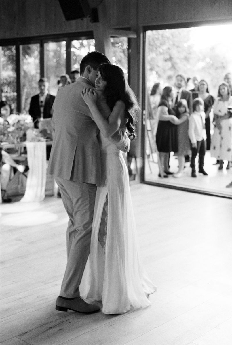 A wedding couple dancing in an indoor venue with large windows and wooden floors.