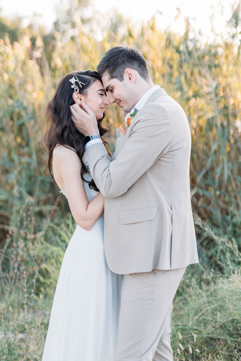 A romantic outdoor wedding photoshoot with a couple embracing in a field at sunset.