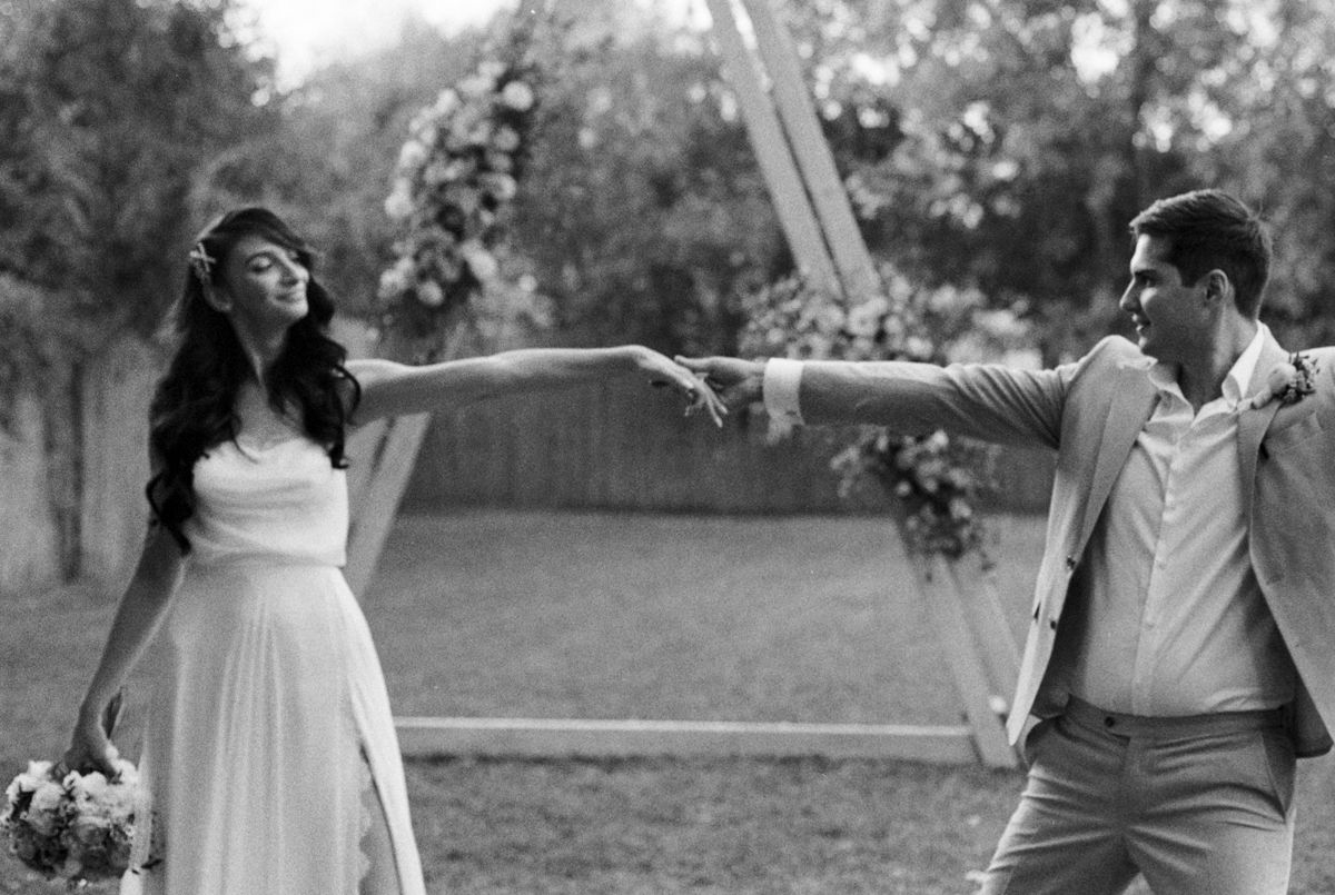 A couple shares intimate moments outdoors near a wooden ceremony arch.